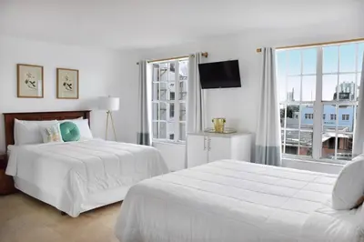 a white bedroom with two beds and a window at Beach Park Hotel in Miami Beach