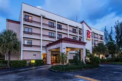 a large white building with palm trees in front of it at Red Roof PLUS Miami Airport in Miami