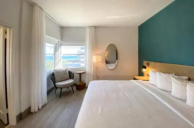a bedroom with a bed and a chair and a window at Marseilles Beachfront Hotel in Miami Beach