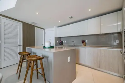 a kitchen with white cabinets and a counter and two stools at Amazing views on the 29th floor 2BR Beach Resort in Hallandale Beach