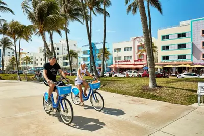 two people riding bikes down a sidewalk with palm trees at Rock Apartments by Lowkl in Miami Beach