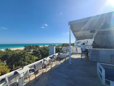 a man sitting at a bar on a deck with the beach at VERSACE MANSION VIEW SUITE at THE STRAND in Miami Beach