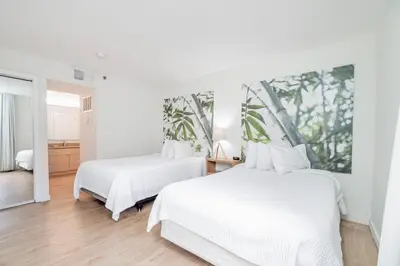two beds in a bedroom with white walls and wood floors at Doral Inn & Suites Miami Airport West in Miami