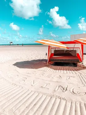 a beach with two umbrellas and a bench on the sand at B Ocean Resort Fort Lauderdale Beach in Fort Lauderdale