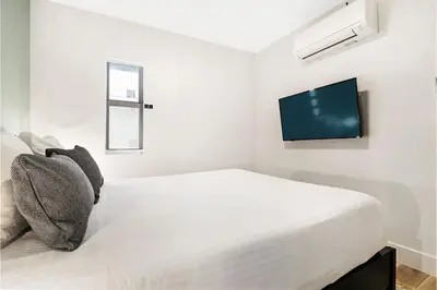 a white bedroom with a bed and a flat screen tv at Roami at The Carmela in Miami Beach