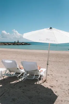 two people sitting in chairs under an umbrella on the beach at Beach Haus Bal Harbour in Miami Beach