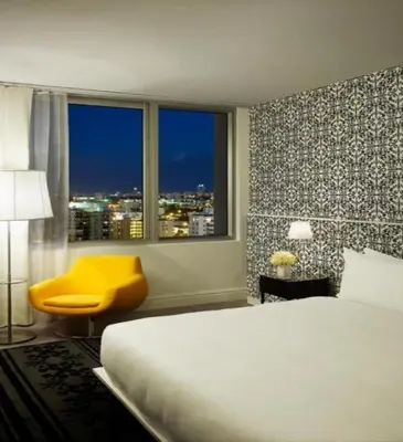 a bedroom with a bed and a yellow chair and a window at Mondrian South Beach in Miami Beach
