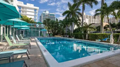a pool with chairs and umbrellas and palm trees at Best Western Plus Oceanside Inn in Fort Lauderdale