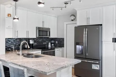a kitchen with white cabinets and a stainless steel refrigerator at Tranquil Retreat with HEATED POOL Minutes to the Beach in Dania Beach