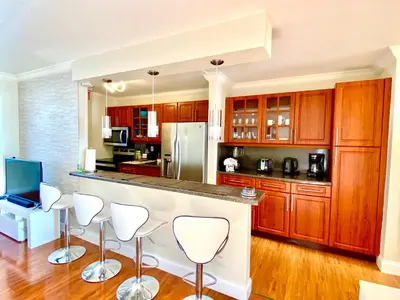 a kitchen with wooden cabinets and a counter with white bar stools at Deluxe waterfront one bedroom apartment with Miami Skyline view, free parking 5 mins drive to Miami Beach in Miami Beach