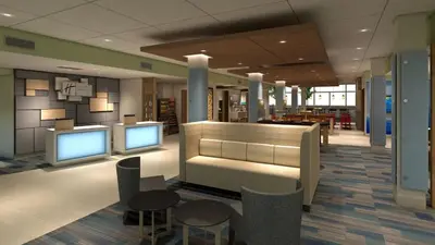 a lobby with two monitors and tables and chairs at Holiday Inn Express & Suites - Miramar by IHG in Miramar