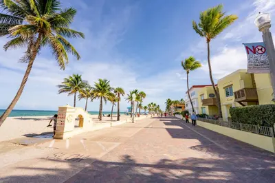 a sidewalk on the beach with palm trees and the ocean at The Surf Hollywood Beach in Hollywood