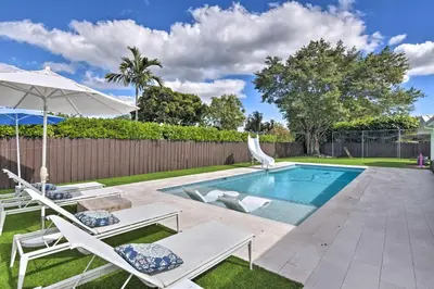 a swimming pool with two chairs and an umbrella at Miami Home Outdoor Pool with Slide and Fire Pit! in Kendall