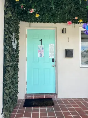 a blue door on a white house with flowers at Stunning Little Havana Suites Close to airport, Calle Ocho, Brickell, Wynwood and the Beaches - Free Parking in Miami