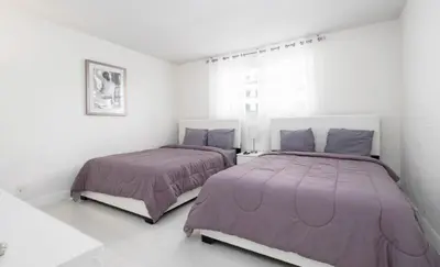 two beds in a bedroom with white walls and purple blankets at Beautiful 2 Bedroom Apartment on Hollywood Beach in Hollywood