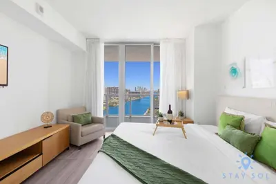 a white bedroom with a large bed and a window at Infinite View, Balcony, Gym, Amazing Pool in Hallandale Beach