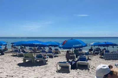 a group of people sitting on a beach with blue umbrellas at Boutique-Style Miami Apt, Comfort, Design & Sea View -26A in Hallandale Beach