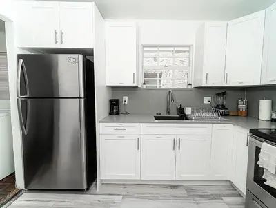a kitchen with white cabinets and a stainless steel refrigerator at Bike to Beach-Spacious With Patio BBQ & Game Room (Pet-Friendly) in Hallandale Beach