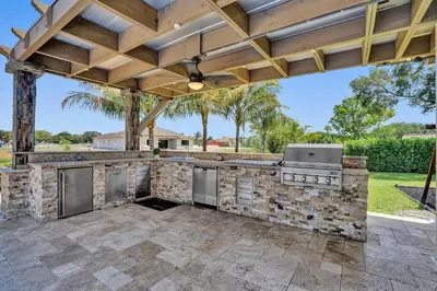 an outdoor kitchen with a stone wall and a wooden pergola at Villa wpool mini-golf firepits in Davie
