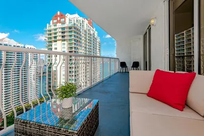a white couch on a balcony with a red pillow at Lovely condo with city & ocean views. Sleep up to 6 people! in Miami