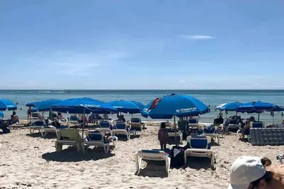 a group of people sitting on a beach with umbrellas at Beachfront Apartment in Miami Beach with Stunning Views 1A in Hallandale Beach