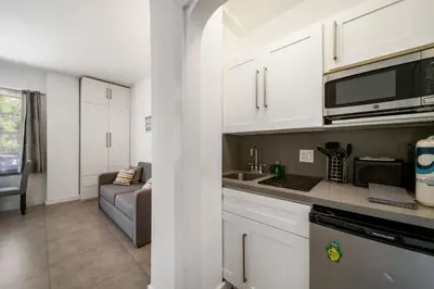 a kitchen with white cabinets and a couch in a room at Beach Bae -Deco Studio Steps from the Ocean in Miami Beach