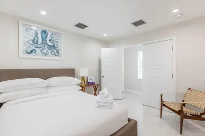 a white bedroom with a bed and a chair at Olas Villa by Rove Travel - Home with Heated Pool in Fort Lauderdale