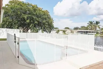a white fence with a pool in front of the water at Stunning Lake-Front Villa with Pool & Spa in Pembroke Pines