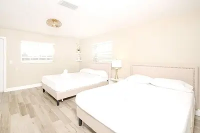 two beds in a bedroom with white walls and wooden floors at Stunning Lake-Front Villa with Pool & Spa in Pembroke Pines