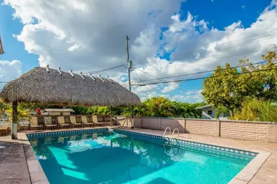 a swimming pool with a thatch roof and a swimming pool at Beautiful 7-Bedroom Villa with Pool in Hialeah