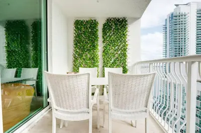 a balcony with white chairs and a green hedge at Ocean and City Views Lux Miami Brickell Condo Sleeps 4, King Bed in Miami