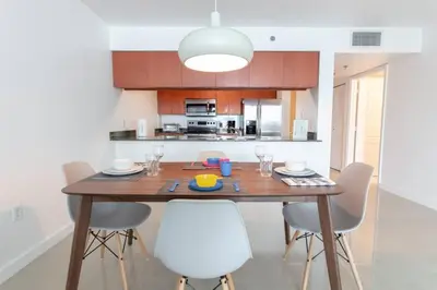 a kitchen with a wooden table and white chairs at Sunshine Ocean and City Views 1 BR Paradise with Parking in Miami