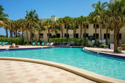 a swimming pool in front of a building with palm trees at Beachfront 1-Bedroom Apartment with Ocean View, Pool and Gym in Hollywood Beach in Hollywood