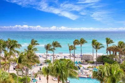 a view of a beach with palm trees and the ocean at Beachfront 1-Bedroom Apartment with Ocean View, Pool and Gym in Hollywood Beach in Hollywood
