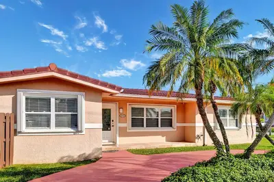 a house with two palm trees in front of it at Deluxe Home Heated Pool & Jetted Tub near Beach in Dania Beach