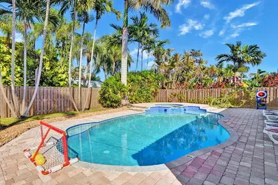 a swimming pool in a yard with a fence and palm trees at Deluxe Home Heated Pool & Jetted Tub near Beach in Dania Beach