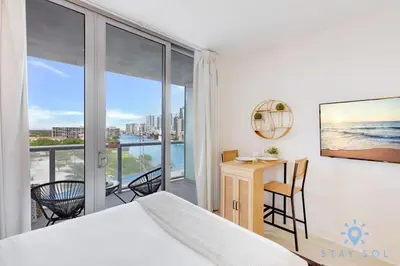 a bedroom with a bed and a desk and a balcony at Pool - Apartment with Balcony - Gym - Near Beach in Hallandale Beach