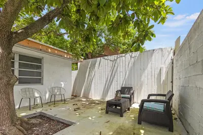 a patio with chairs and a tree next to a wall at Intimate Casita Mia minutes away from Airport, Calle 8, Brickell, Coral Gables, The beach and more! in Miami