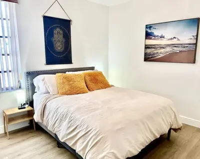 a bedroom with a bed with white sheets and a picture at Lush tropical big home close to Airport, Calle 8, Coral Gables and lots more Miami amenities in Miami