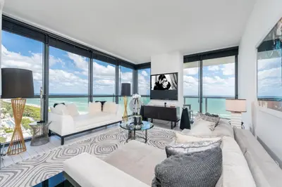 a living room with a couch and a tv and windows at Stunning 3B Oceanfront at South Beach - 1229 in Miami Beach