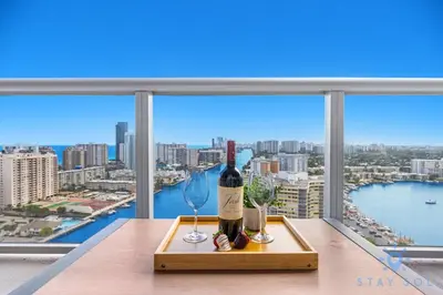 a bottle of wine and glasses on a table in front of a window at Infinite View Balcony Pool in Hallandale Beach