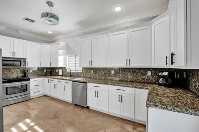 a white kitchen with white cabinets and granite counter tops at Hot Tub! Roof Top! Firepit! Boat Dock! in Fort Lauderdale