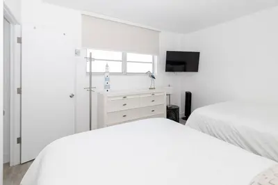 a white bedroom with two beds and a tv at Stunning & Spacious Resort-Style Condo Across From Beach! in Miami Beach