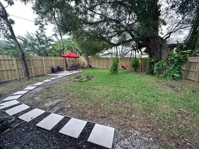 a backyard with a fence and a red umbrella at Enjoy our brand new home close to Hollywood in Hallandale Beach! in Hallandale Beach