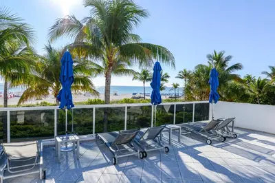a patio with chairs and blue umbrellas and the beach at Decoplage Paradise - Unit B in Miami Beach