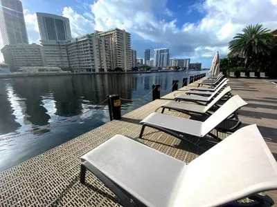 a row of white lounge chairs on a pier next to the water at Modern Beach Apartment, 3 Beds, Views & Full Kitchen in Hallandale Beach