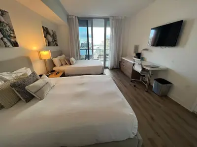 a hotel room with two beds and a desk and a television at Studio BeachWalk, Ocean Breeze & 2 Full Beds in Hallandale Beach